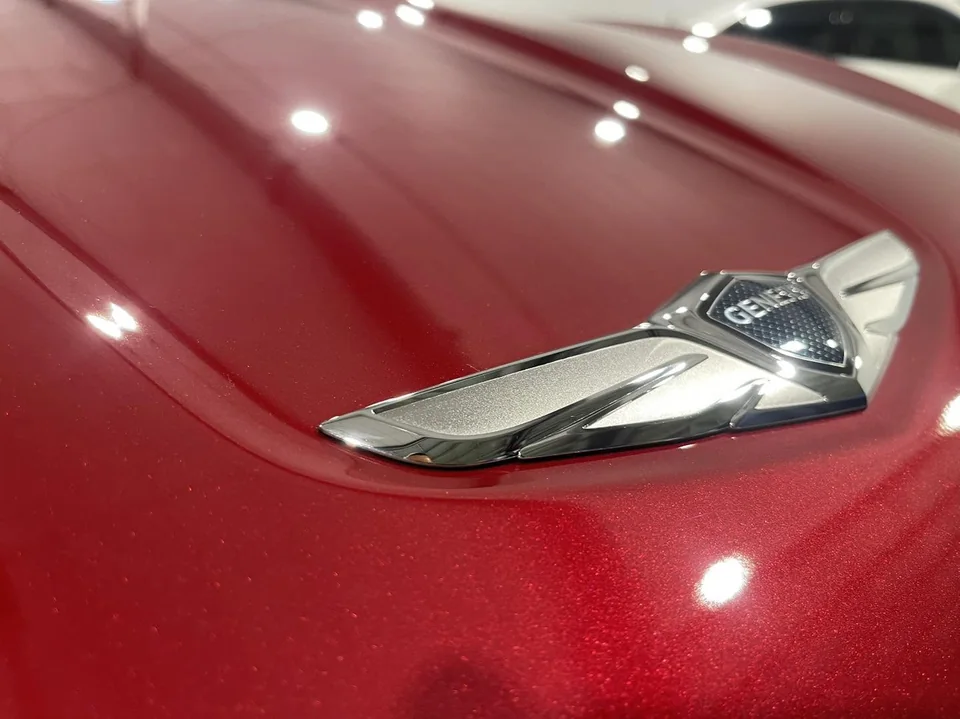 Deep red Genesis hood and chrome badge reflecting the bay lights